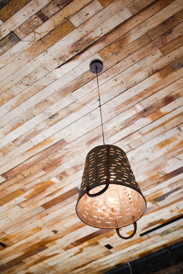 Eine antike Recycling-Lampe hängt von einer Holzdecke