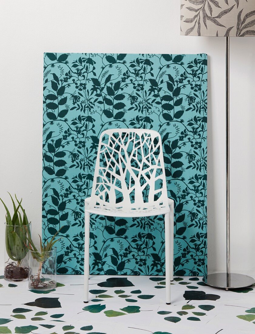 Filigraner weißer Stuhl vor Stoffbezogener Leinwand im Dschungel-Look und weißem Boden mit Blättermotiven