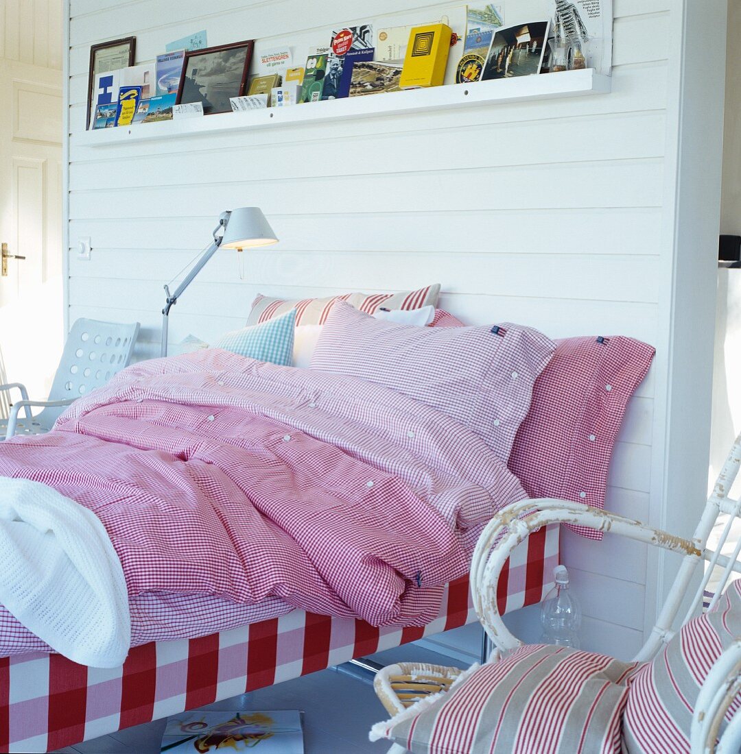 Verscheidene, rot karierte Bettwäsche auf Bett vor weiss vertäfelter Raumteilerwand