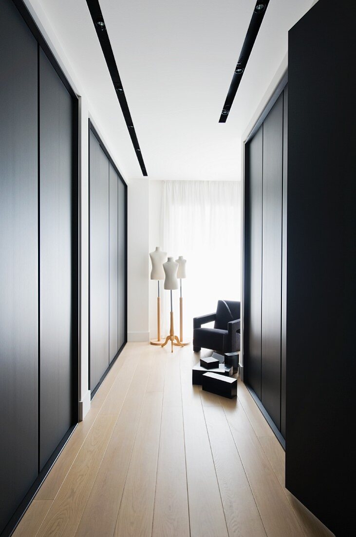 Eleganter Ankleidebereich mit raumhohen schwarzen Einbauschränken, im Hintergrund Schneiderpuppen und schwarzer Sesssel