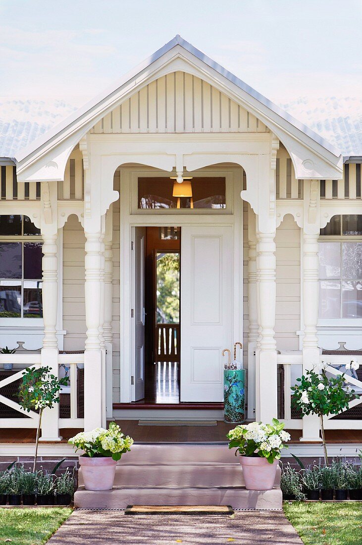 Traditionelles, weisses Holzhaus - Veranda mit gedrechselten Säulen auf Treppenstufen vor teilweise offenem Hauseingang Blumentöpfe