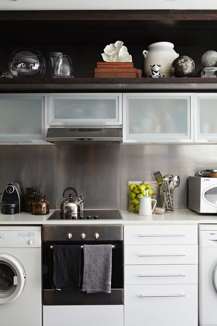 weiße Einbauküche mit Hängeschränken und dunklem Holzboard für diverse Glasgefäße und Sammlerstücke