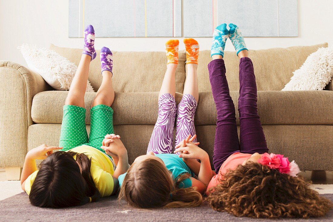 Drei Mädchen vor einem Sofa auf dem Boden liegend mit hochgestreckten Beinen