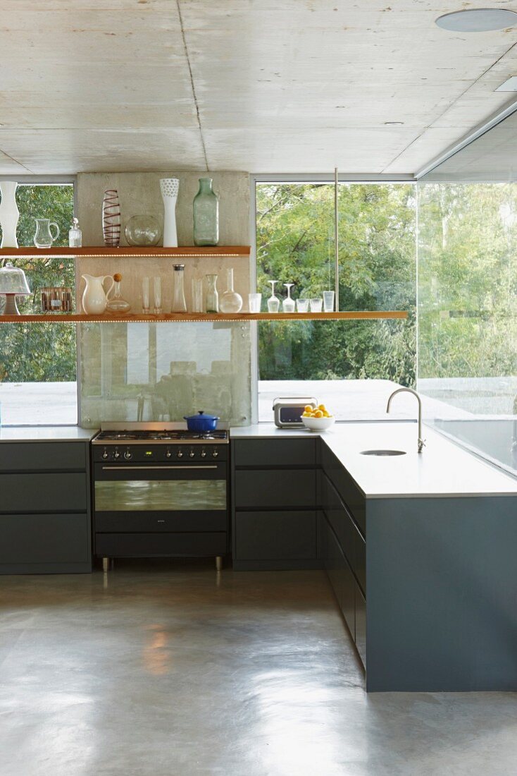Anthrazitfarbene, puristische Küchenzeile mit abgehängten Regalböden vor verglaster Fassade