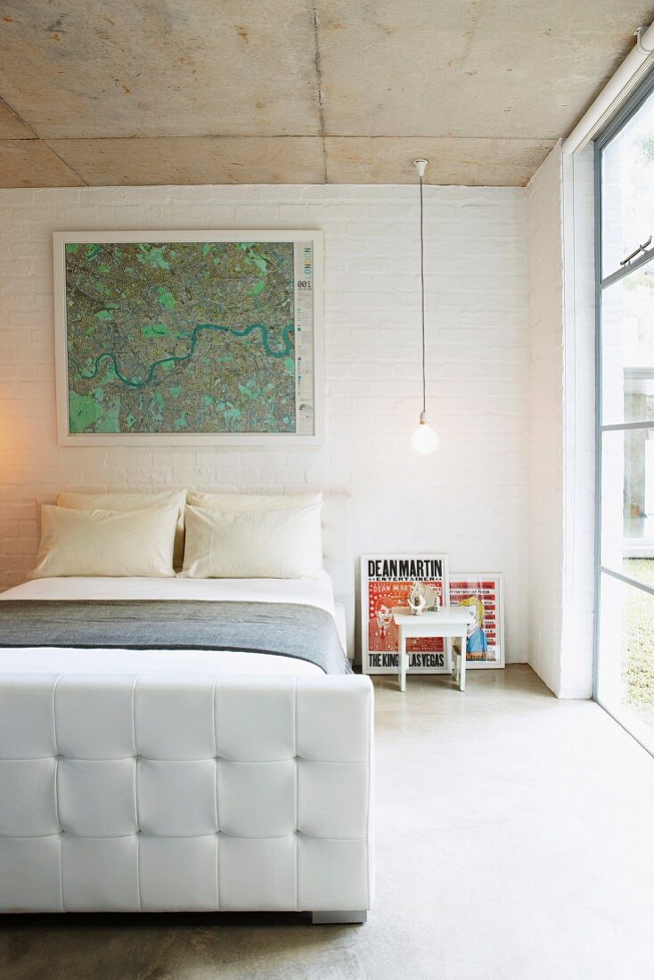 Framed map above French bed in simple bedroom with glass wall