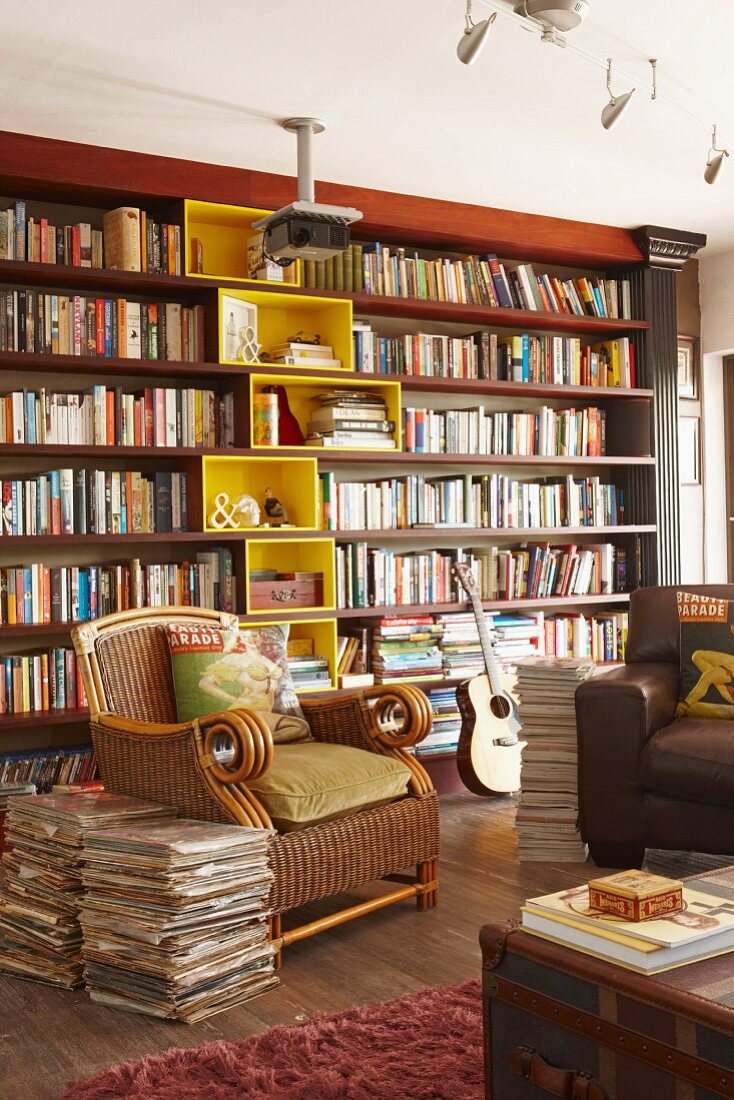 Sessel mit bedruckten Dekokissen und Zeitungsstapel in Stilmix Wohnraum mit Bücherwand