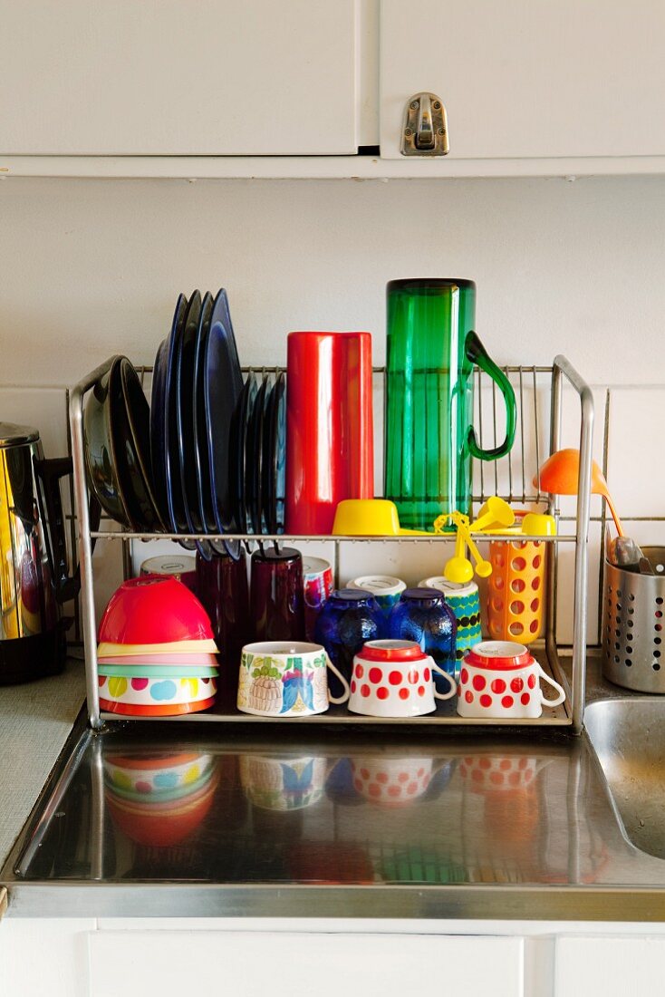 Colourful crockery on metal drying rack on stainless steel sink surround