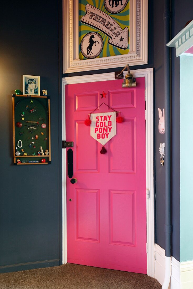 Pink door in hallway painted dark grey with framed poster and pinboard