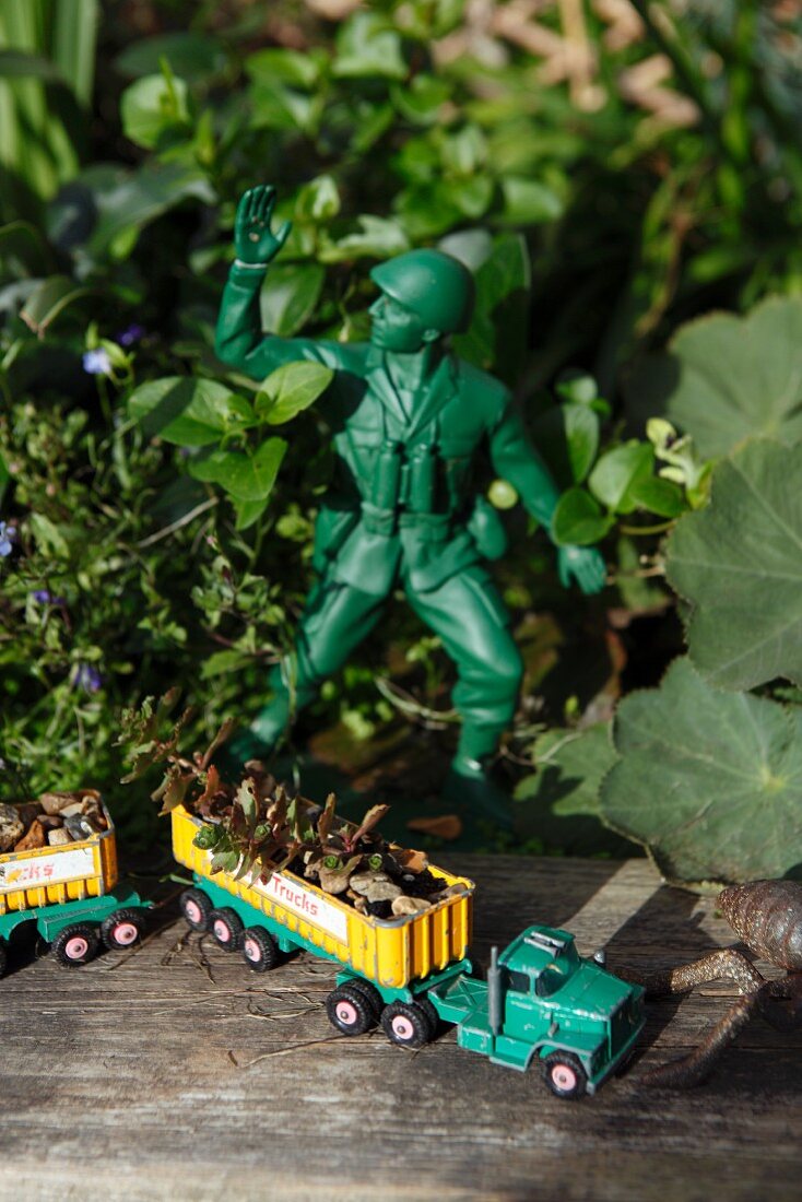 Beladener Spielzeuglastwagen auf verwittertem Holzbrett im Garten mit Soldatenfigur