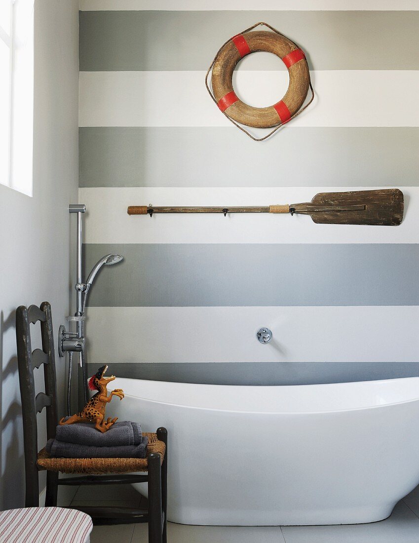 Modern bathroom with free-standing bathtub and maritime decorations on grey and white striped wall