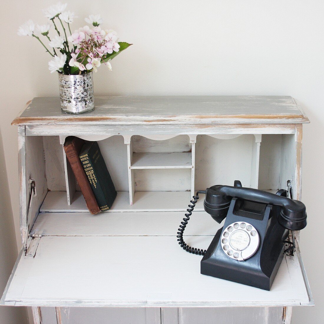 Old telephone, books & flowers on open, white bureau