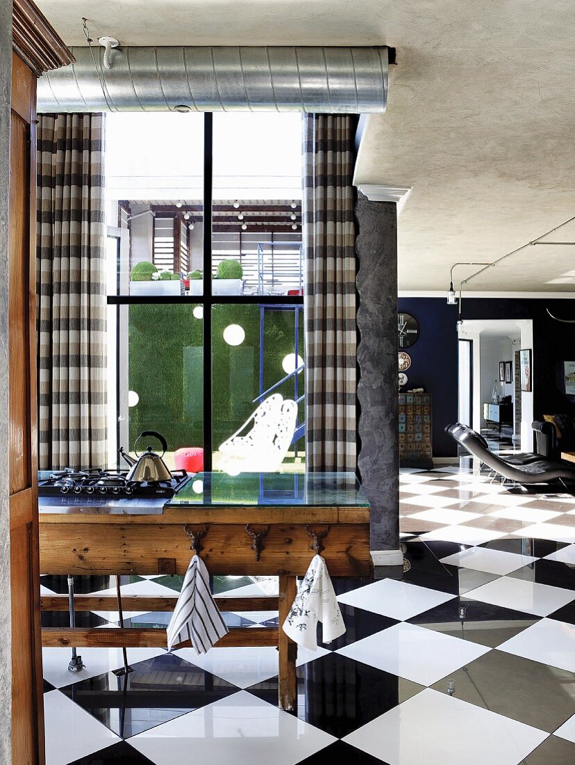 Improvisierte Kochinsel aus alter Werkbank mit Gasherd in offenem Wohnraum mit eleganten Schachbrettfliesen