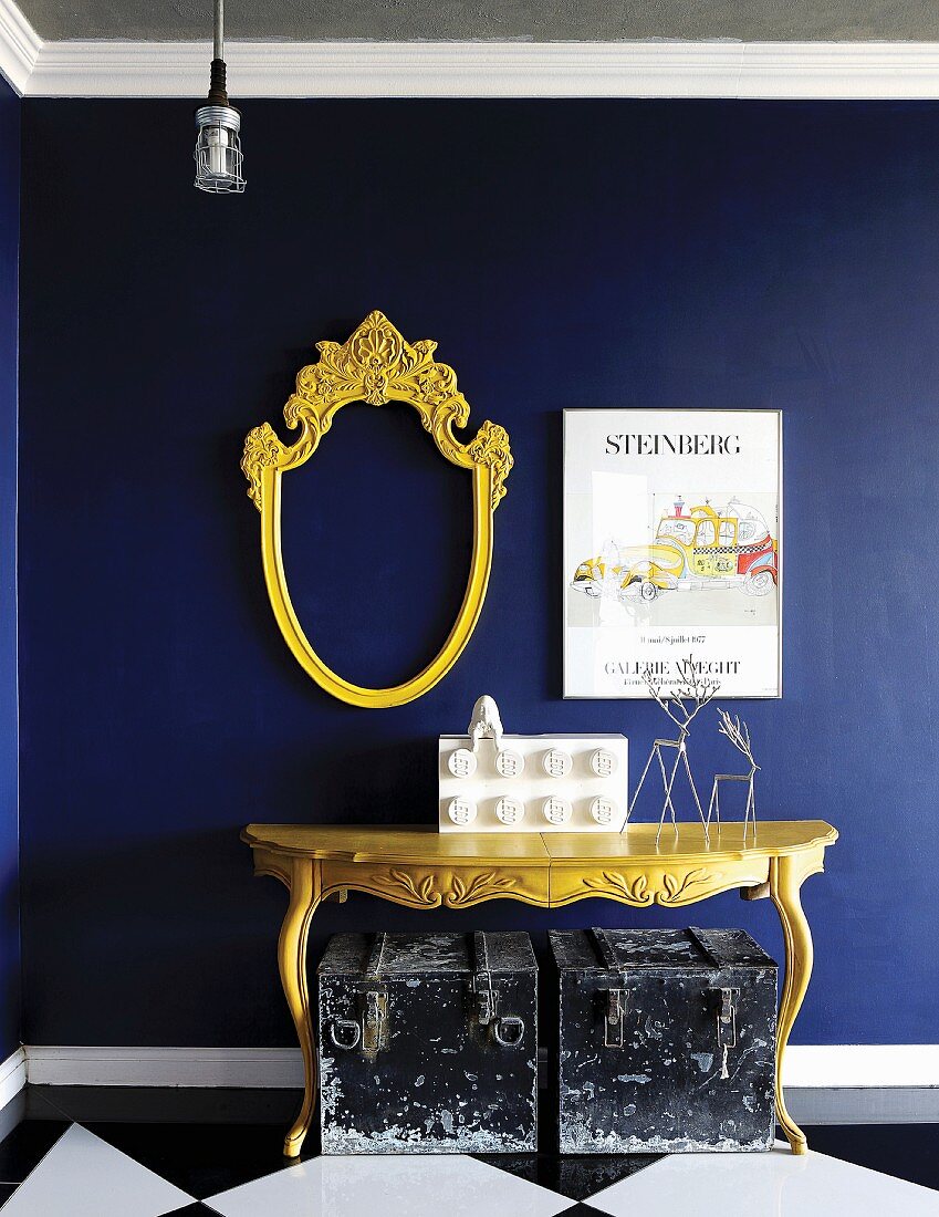 Gelber Konsolentisch und wappenartiger, leerer Spiegelrahmen vor königsblauer Wand