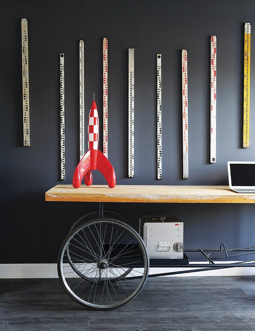 Tintin rocket on upcycled table with wheels below collection of old rulers hanging on dark wall