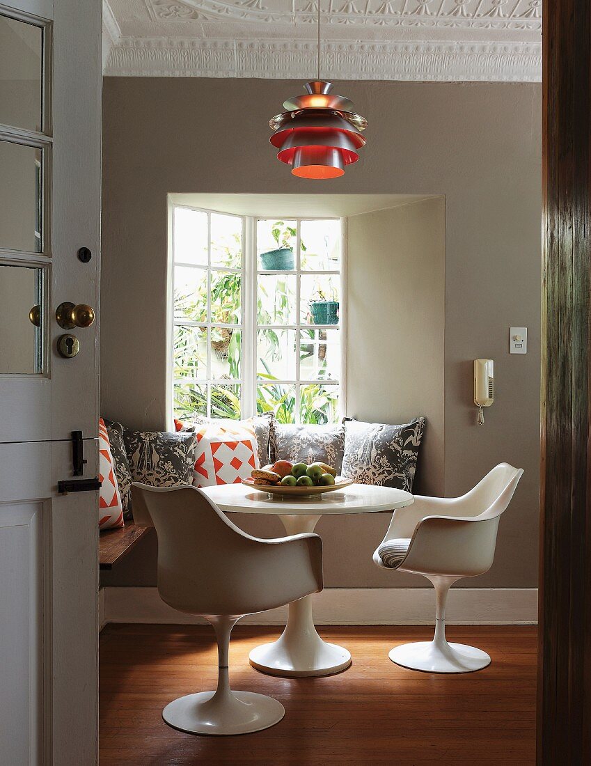 Classic, white swivel chairs and round table in front of bench with many scatter cushions below classic pendant lamp hanging from stucco ceiling
