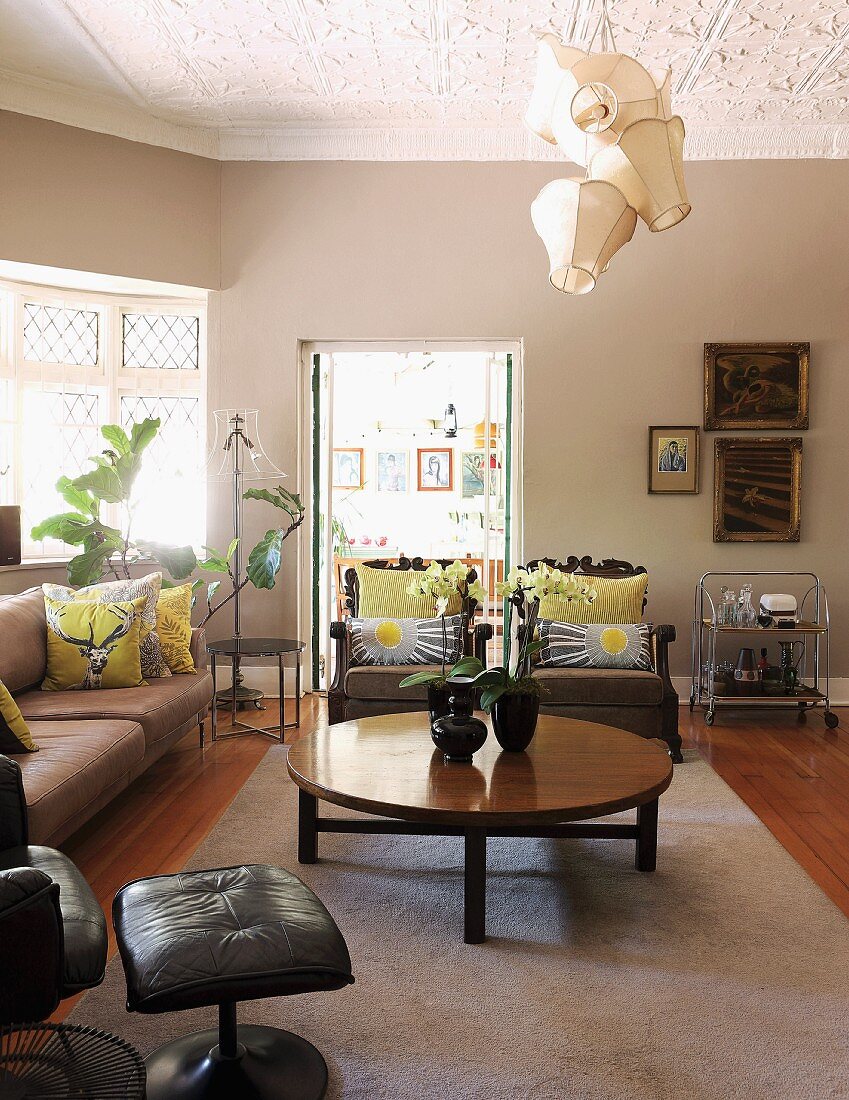 Runder Couchtisch auf hellem Teppich und Sofagarnitur in elegantem Wohnzimmer, an Stuckdecke verspielte Pendelleuchte mit traditionellen Stoffschirmen
