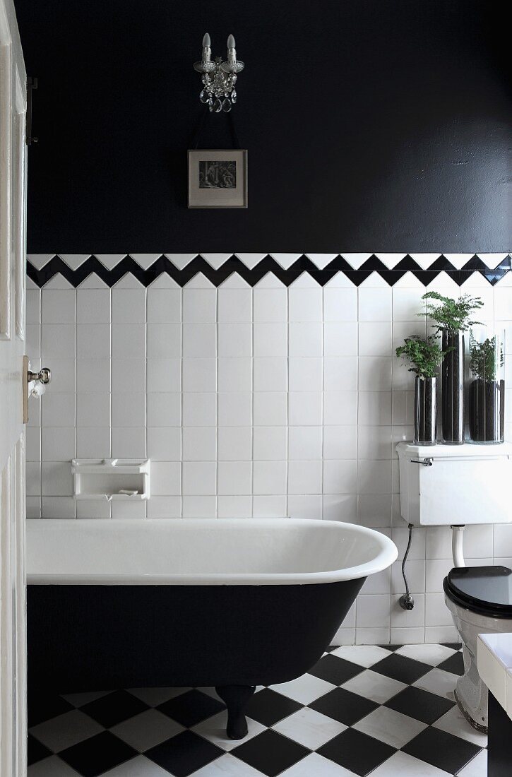 Blick durch offene Tür in schwarzweisses Bad - Vintage Badewanne auf Schachbrettmusterboden vor halbhoher, weisser Fliesenwand abgesetzt durch Bordüre von schwarzer Wandfläche