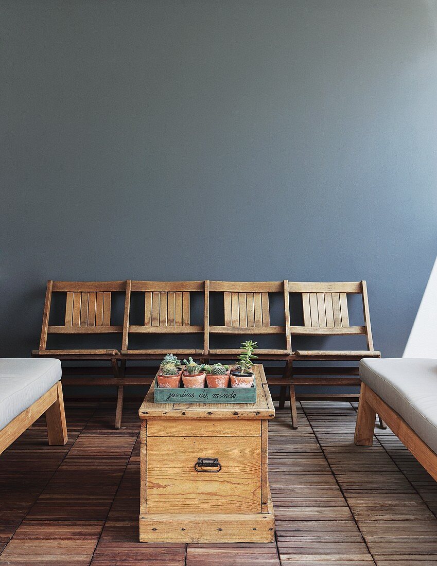 Alte Kinostühle an blauer Wand; im Vordergrund eine einfache Holztruhe zwischen gepolsterten Sitzbänken