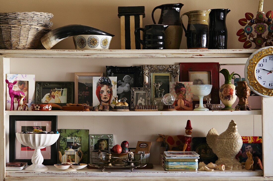 Weisses Regal im Shabby Stil mit einer Sammlung gerahmter Fotos, Keramikvasen und einem Tierhorn
