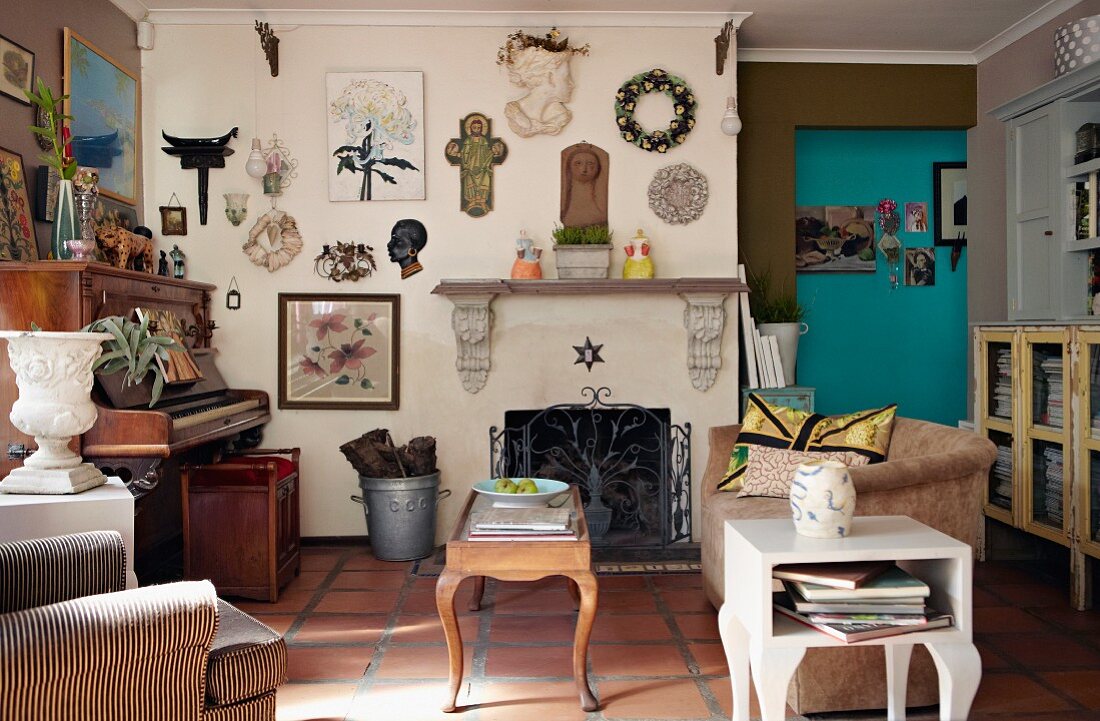Wohnzimmer mit antikem Klavier, Vintage Möbeln und eine mit Sammelstücken dekorierten Wand über offenem Kamin mit schmiedeeisernem Gitter