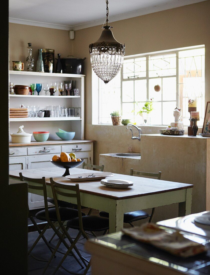 Einfache Küche mit langem Holztisch, einem Geschirrschrank im Vintagelook und einer gemauerten Spüle unter dem Fenster