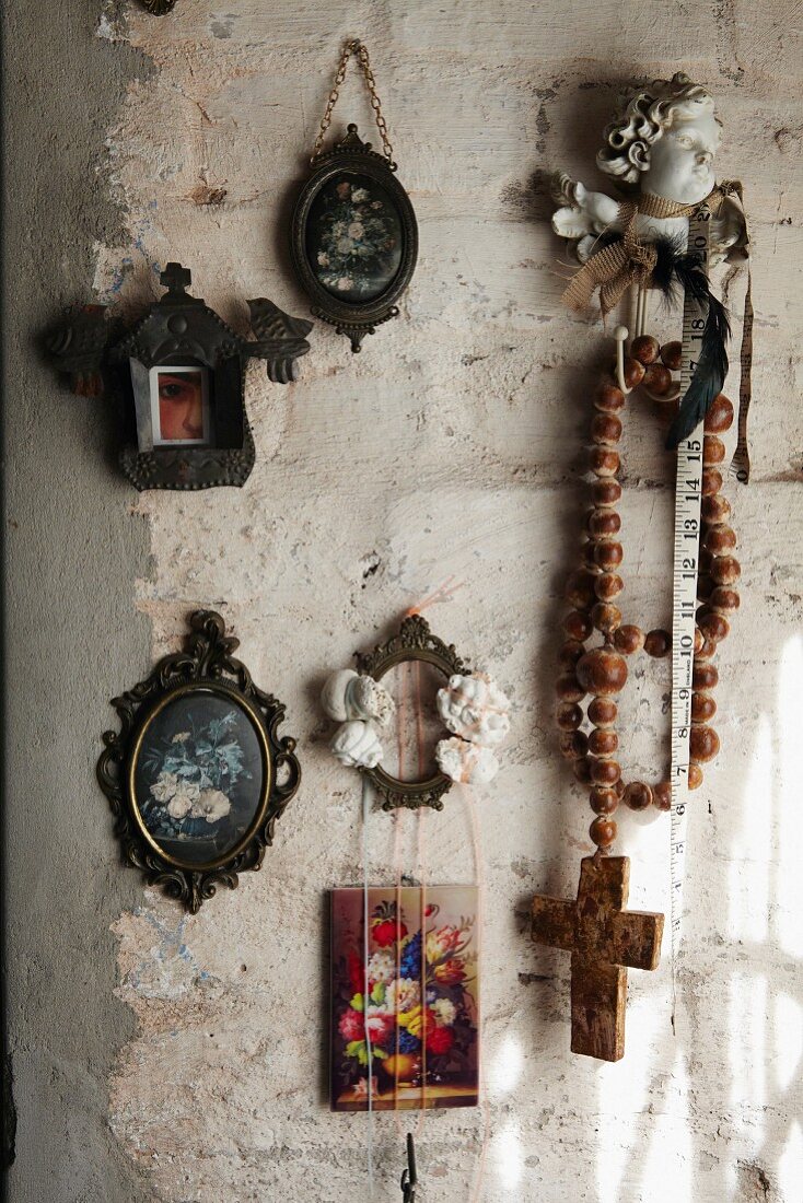 Miniature pictures of flowers and rustic rosary on roughly plastered wall
