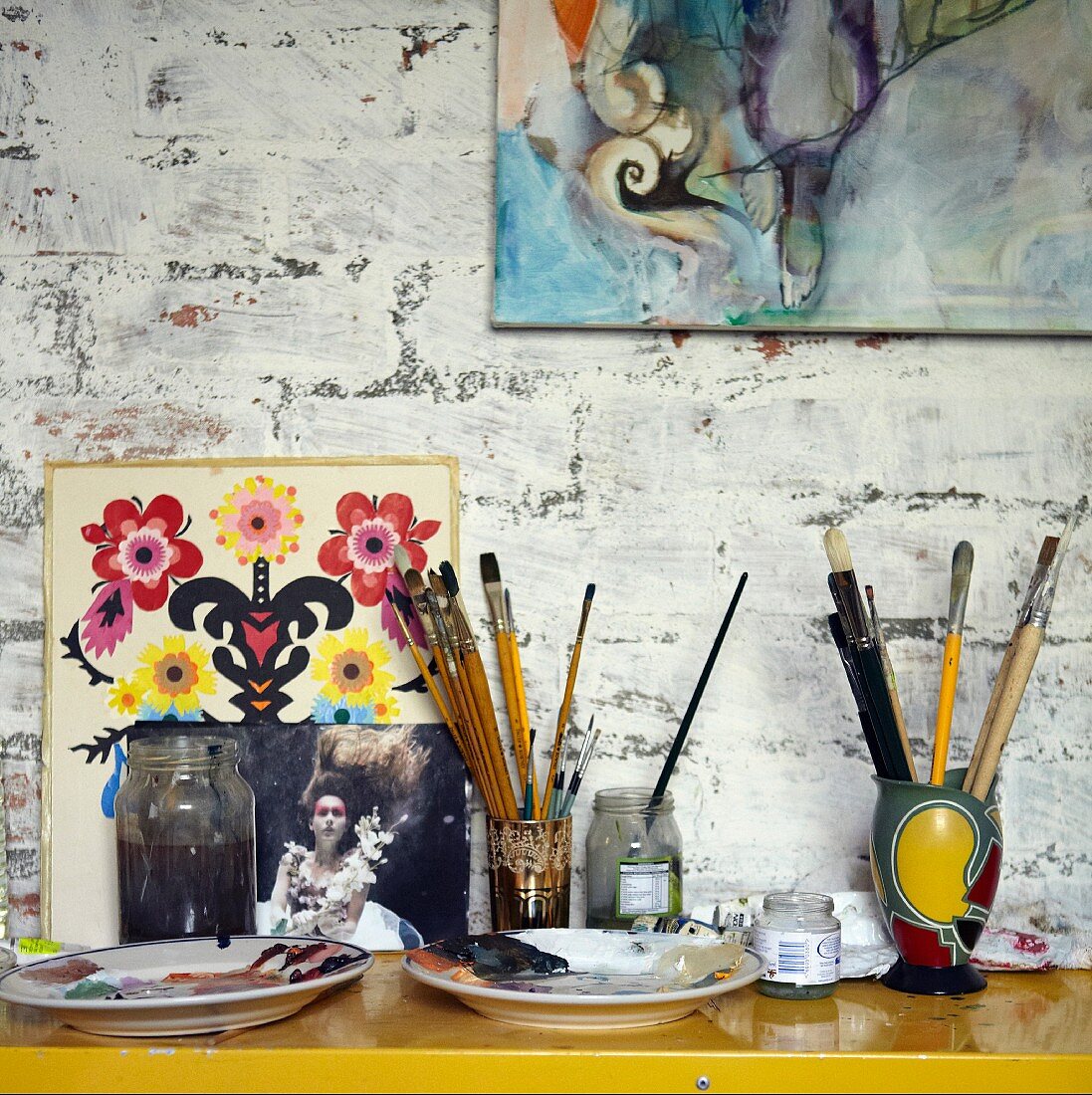Wandtisch mit Malutensilien und angelehnten Bildern an rustikaler Wand