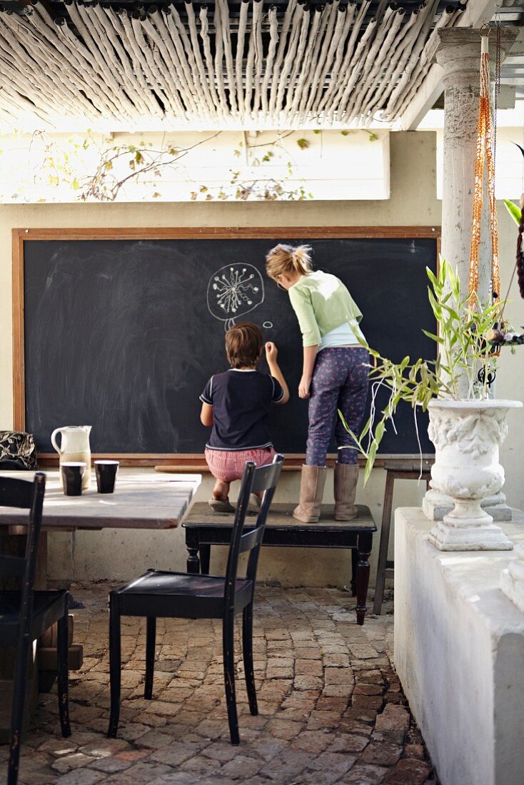 Veranda with vintage furniture and two children drawing on large blackboard