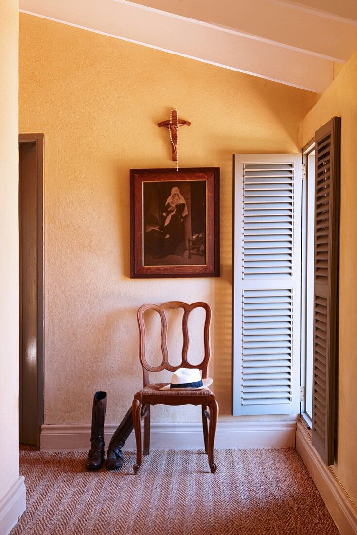French, oak chair below religious painting and crucifix next to window with open shutters