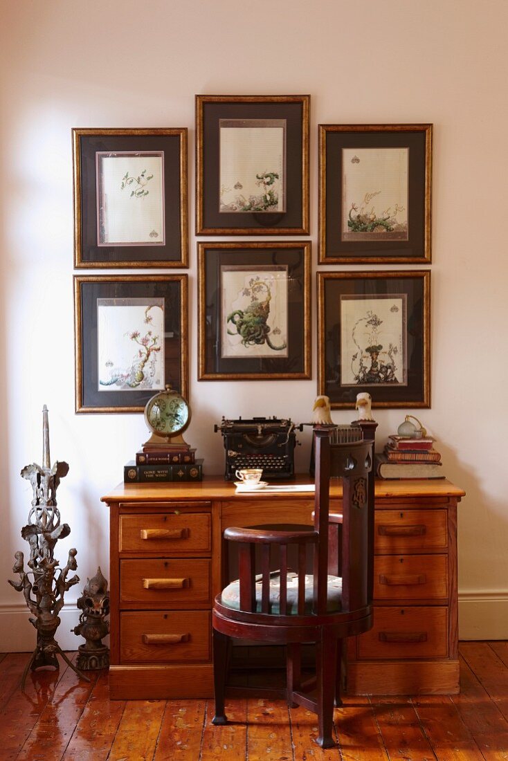 Antiker Stuhl aus dunklem Holz vor Schreibtisch mit Schubladen vor Wand und gerahmten Bildern