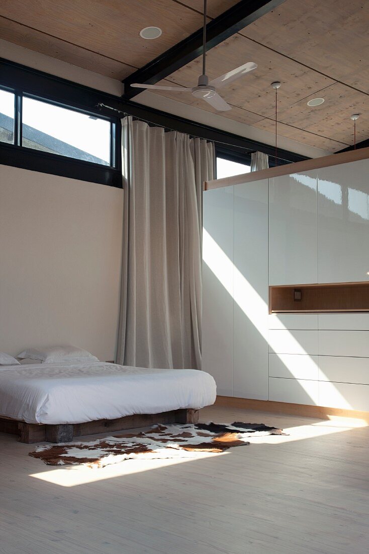 Sleeping area with double bed and cow-skin rug next to wardrobe functioning as partition in contemporary house with transom windows