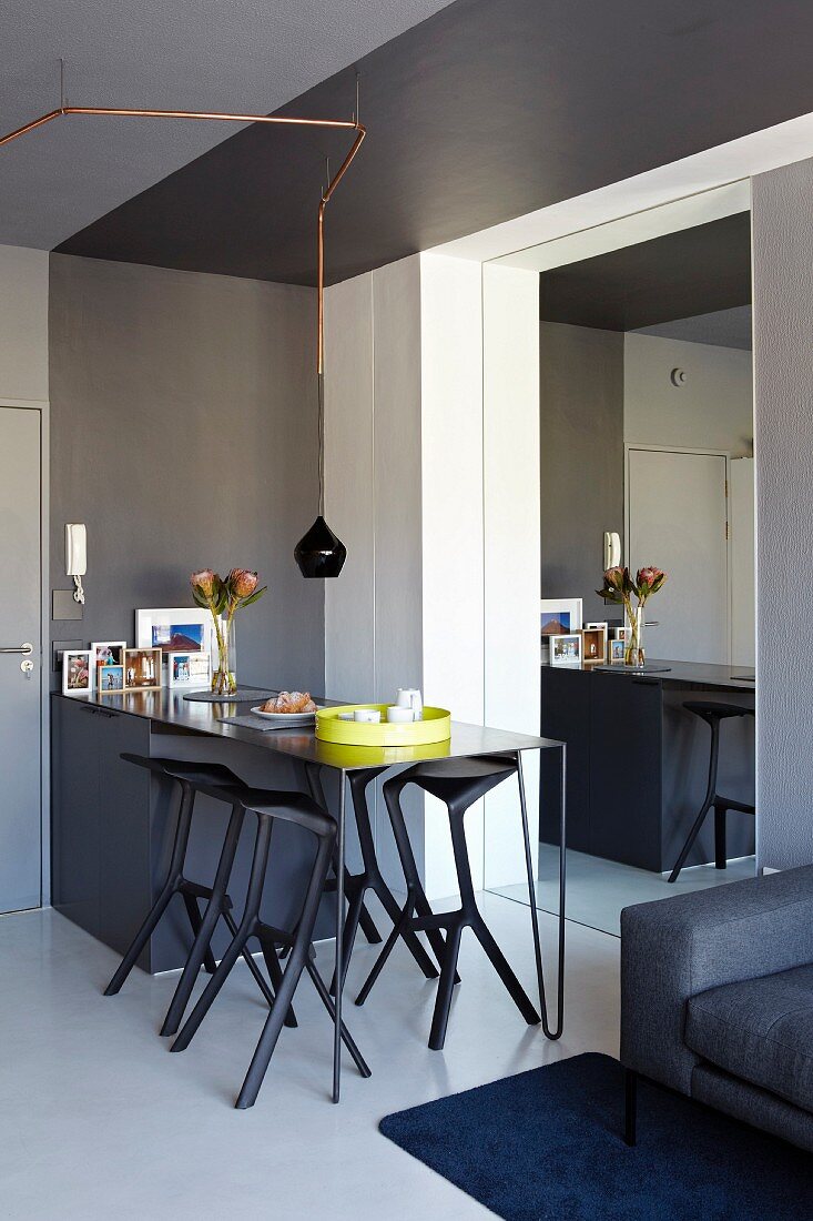 Schwarze Esstheke mit Thekenstühlen neben Eingangstür in modernem Apartment; eine verspiegelte Wand öffnet den Raum