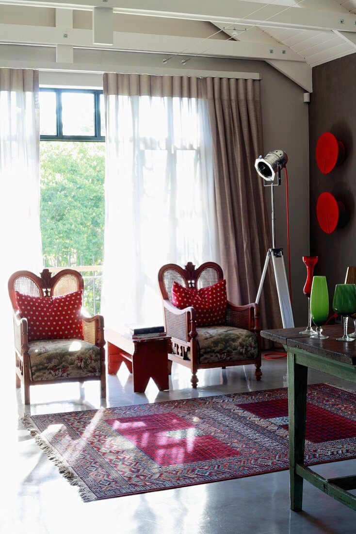 Zwei Sessel mit weiss-rot gepunkteten Kissen vor Fensterfront und Orientteppich auf glänzendem Estrichboden