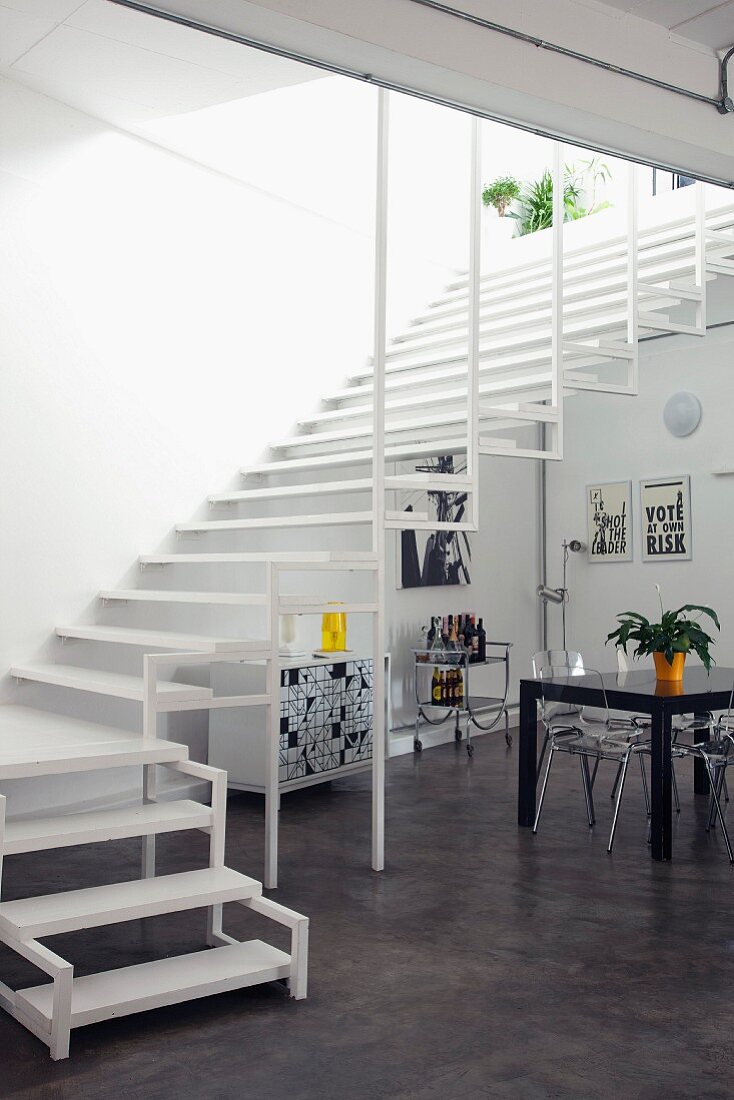 Wide, airy staircase in open-plan interior with designer plexiglass chairs and black dining table; black and white graphics on wall