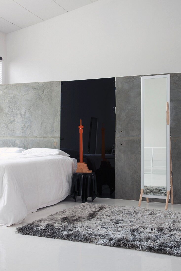 Minimalist gallery bedroom with grey flokati rug and large, full-length mirror against grey partition
