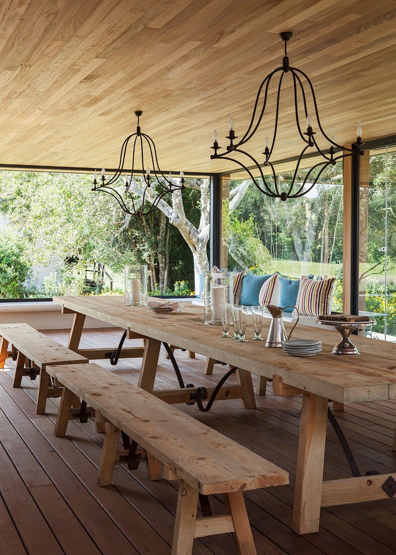 Gemütlicher Essraum mit großen Glasfronten und rustikalen Holzmöbeln; von der Decke hängen schmiedeeiserne Kronleuchter