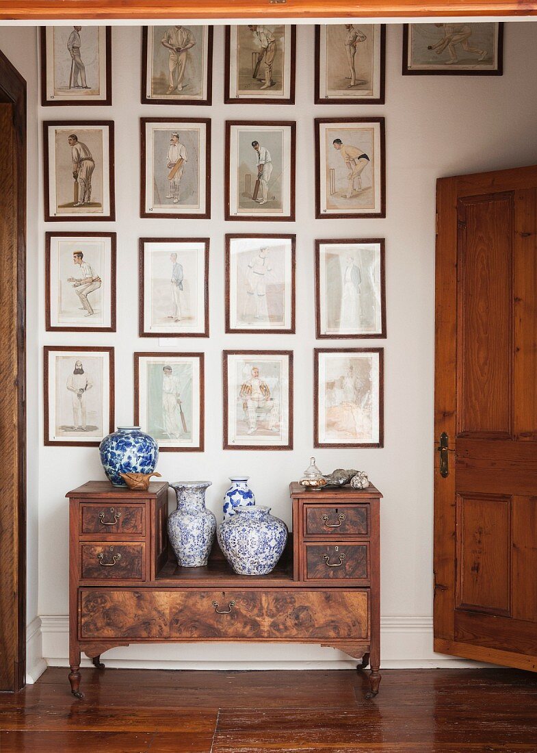 China vases on antique bench below collection of framed drawings on wall