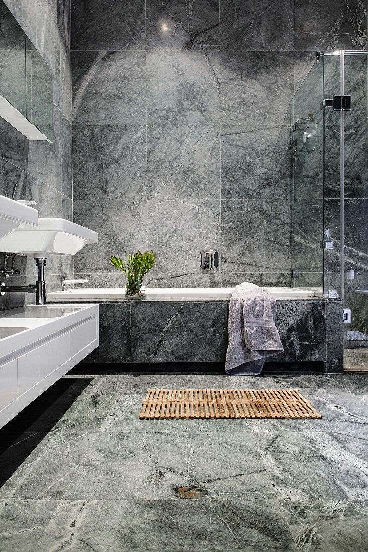 Luxuriöses Badezimmer mit grauen Marmorfliesen und einer Holzmatte vor der Badewanne