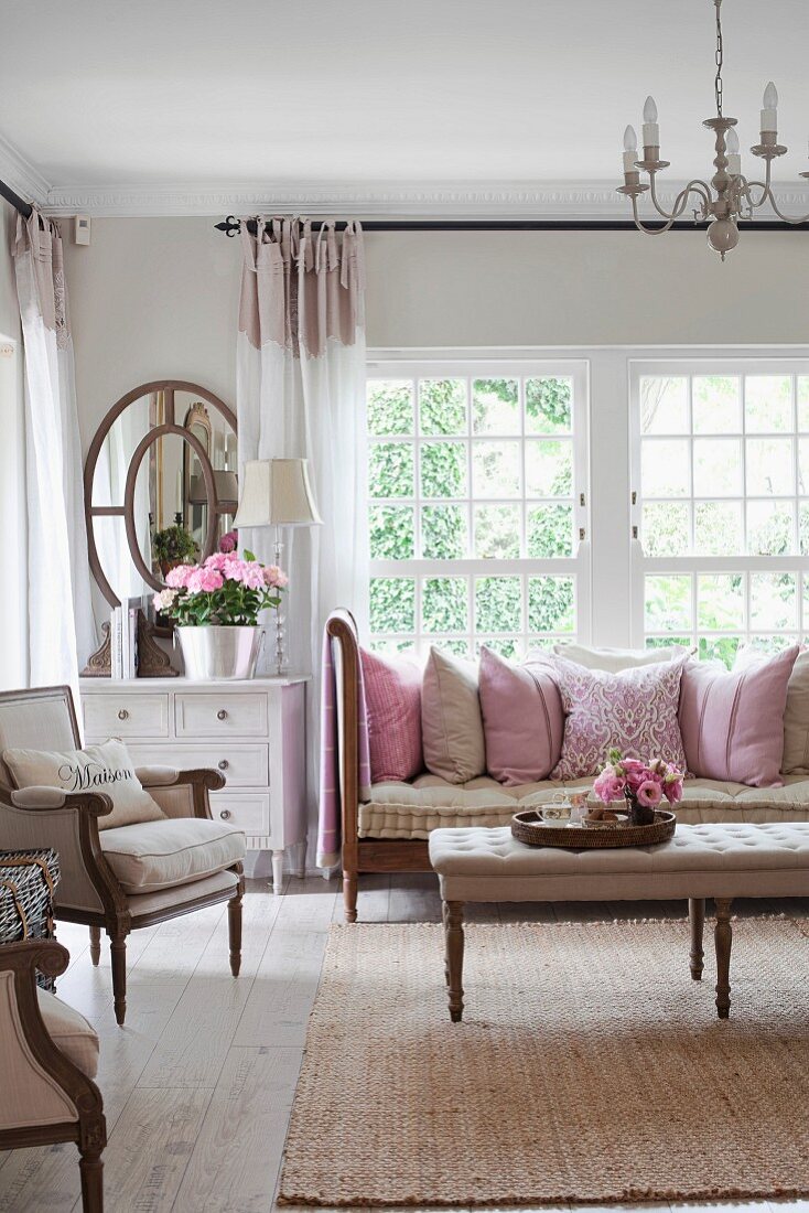 Ein Hauch von Rosa in gemütlichem Wohnzimmer mit weichen, großen Kissen auf dem Sofa und sommerlicher Blumendekoration