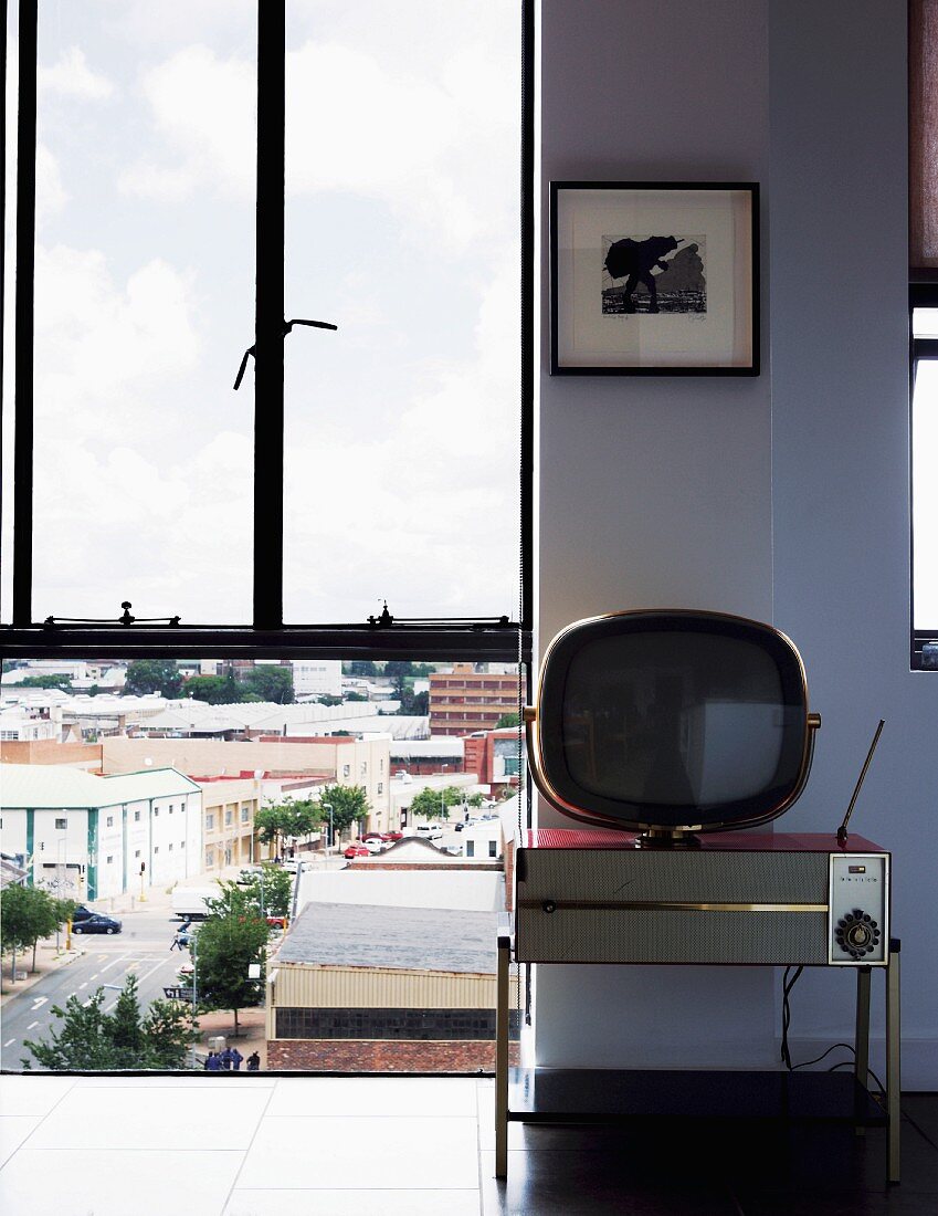 Floor-to-ceiling window with view of cityscape; retro radio and retro TV against wall
