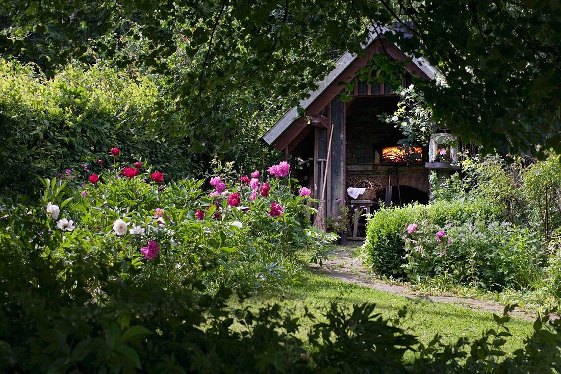 Summer garden with flowering plants and wood-fired bread oven in hut
