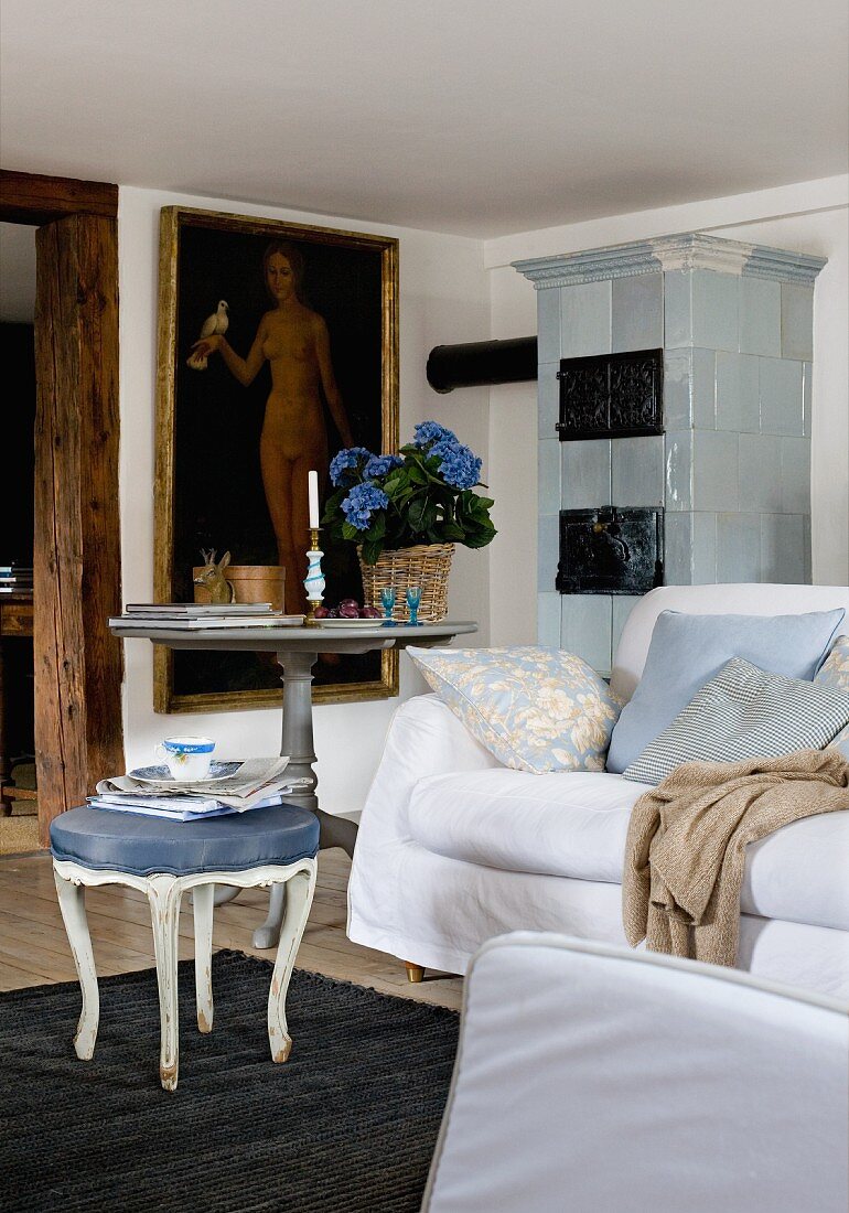 Side table, Rococo footstool, white couch and large, gilt-framed oil painting next to old tiled stove in background