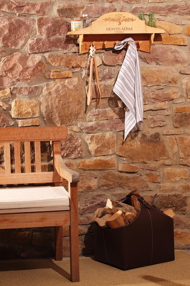 Shelf with hooks upcycled from old wine crate above bench and bag of firewood against rustic stone wall
