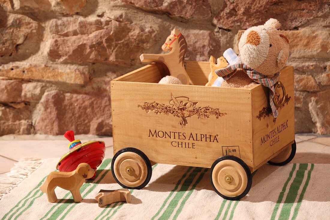 Wine crate on rollers for toy storage in front of rustic stone wall