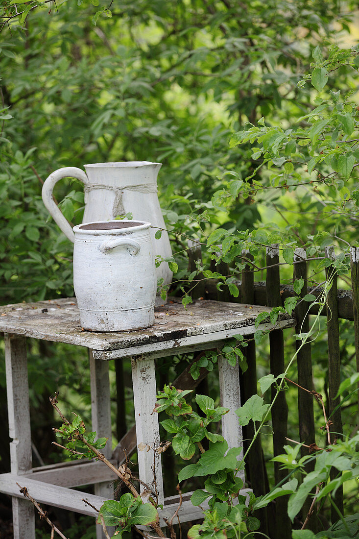 Tontopf und Krug auf einem alten Tisch im Garten am Zaun