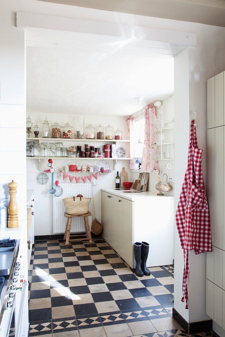 Romantische, weiße Küche mit pinkfarbenen Accessoires und Vorratsgläsern auf Regalborden; historischer Fliesenboden im Schachbrettmuster