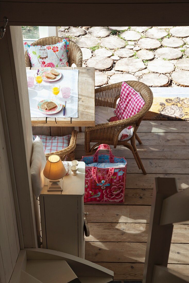 Blick von Treppe auf kleinen Frühstücksplatz mit freundlich gemusterten Kissen in Korbstühlen; Hirnholzterrasse im Hintergrund