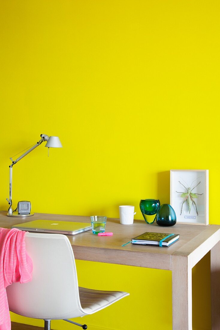 Homeoffice vor leuchtend gelber Wand mit Holzschreibtisch und weißem Bürostuhl