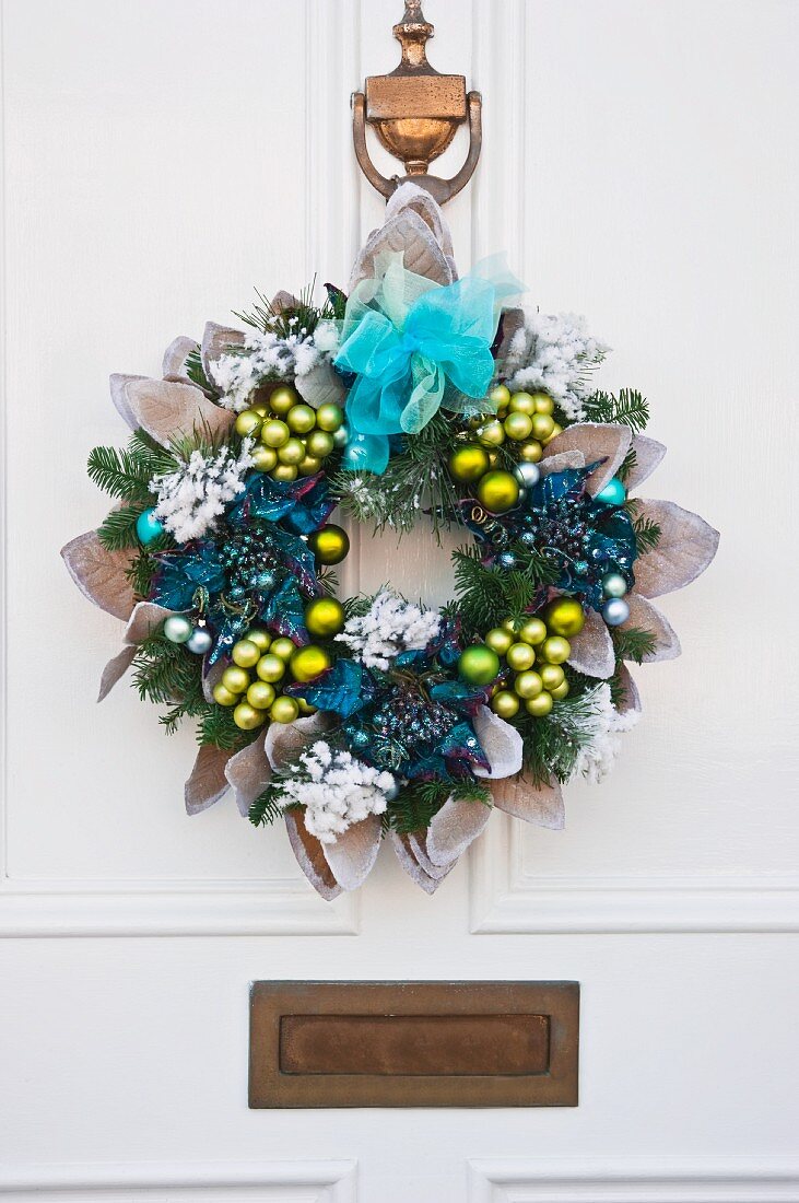 Blue and green fake flower Christmas wreath with baubles and chiffon bows on a white front door