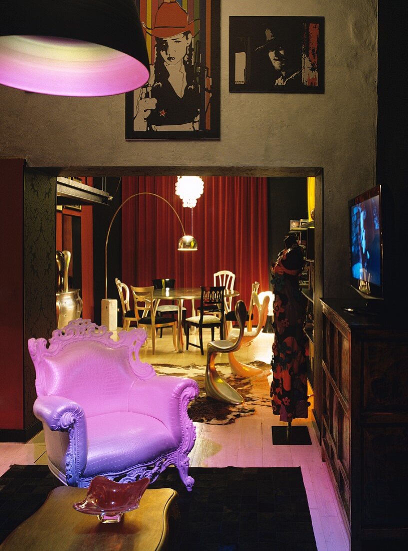 Neo-baroque leather armchair illuminated by pink light; gilt dining table and various chairs in background